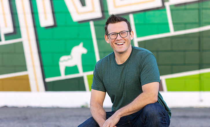 Chris Michel, Muralist, Crouching in front of Aerial Kingsburg Mural